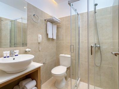 Baño moderno con ducha de vidrio, lavabo, inodoro y toallas en una habitación de hotel.