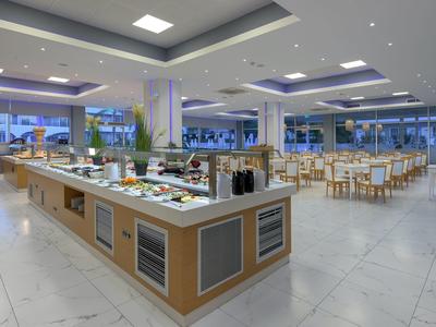 Amplio comedor luminoso con buffet y muchas mesas y sillas en un hotel.