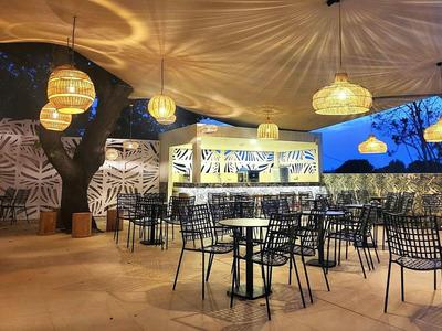 Restaurante al aire libre con muchas sillas y mesas negras de metal bajo luces colgantes cálidas al anochecer.