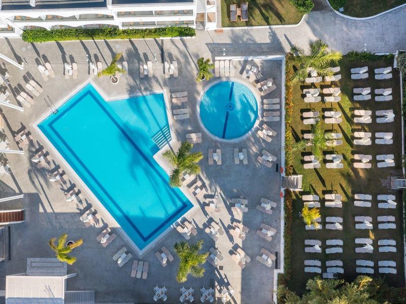 Vista aérea de piscina de hotel con tumbonas y sombrillas junto a área de césped verde.