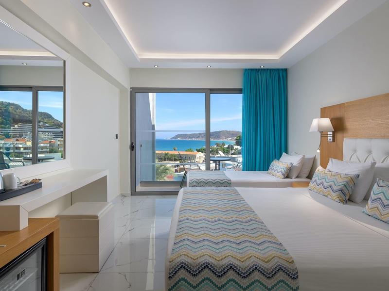 Habitación de hotel moderna con cama doble, vista al mar y gran ventana de vidrio.