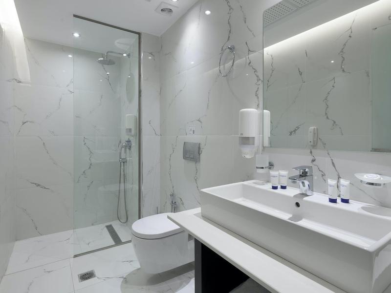 Baño moderno con lavabo doble, ducha de vidrio y paredes blancas con efecto mármol.