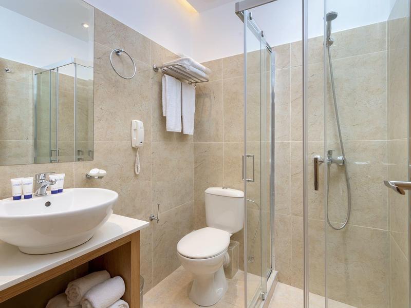 Baño moderno con ducha de vidrio, lavabo, inodoro y toallas en una habitación de hotel.