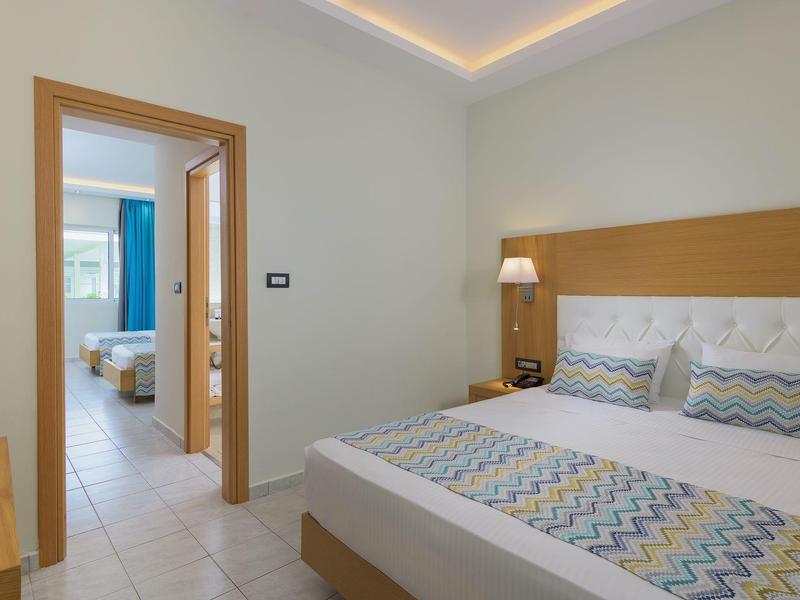 Dormitorio moderno con cama doble y vista a otra habitación con dos camas individuales.