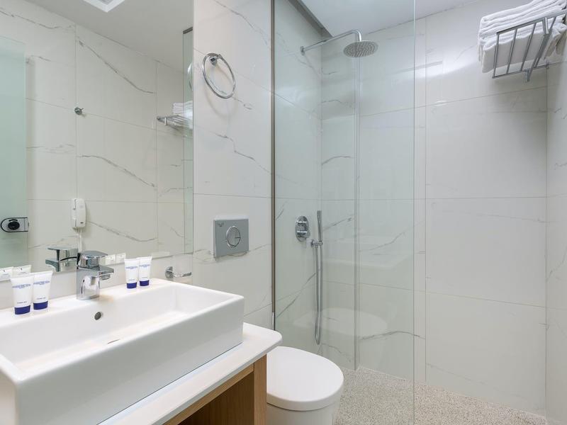 Baño moderno con lavabo doble, ducha de vidrio y paredes blancas con azulejos.