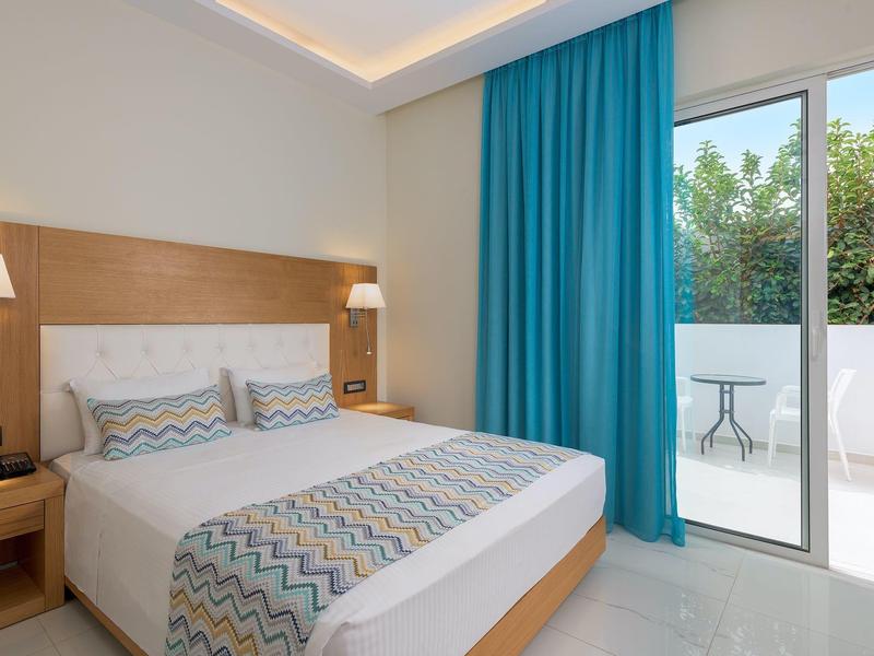 Habitación de hotel moderna con cama doble, cortinas azules y terraza con vista al jardín.