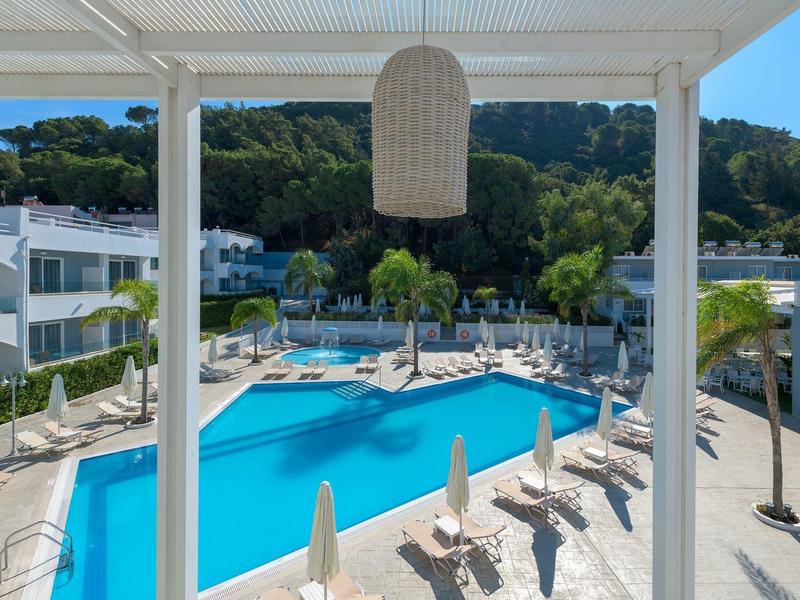 Piscina de hotel moderna con tumbonas y sombrillas ante una colina boscosa bajo cielo despejado.