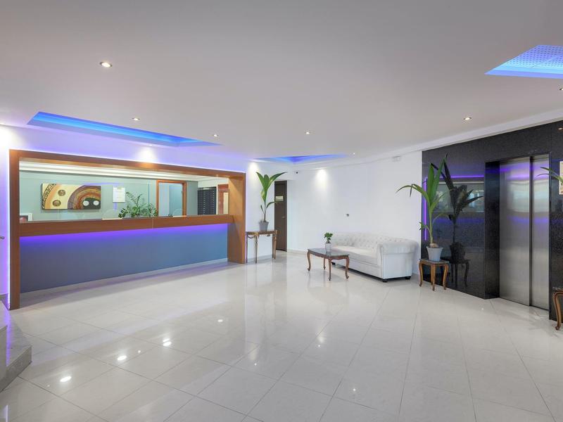 Área de recepción moderna de hotel con mostrador, asientos e iluminación ambiental.