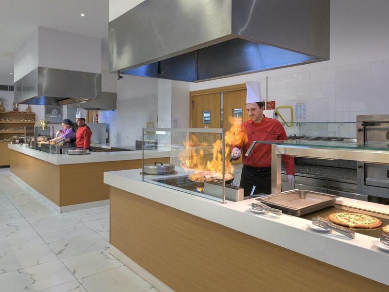 Área gastronómica con chefs preparando pizza frente a fuego abierto.