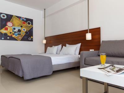 Modernes Schlafzimmer mit Doppelbett, grauer Bettdecke, Sofa, Tisch mit Orangensaft und Kunstwerk an der Wand.
