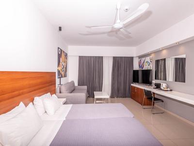 Modernes Hotelzimmer mit zwei Betten, grauem Sofa, Ventilator und großem Spiegel an der Wand.