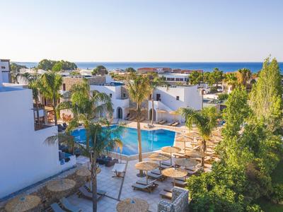 Hotelanlage mit blauen Pools, Palmen, weißen Gebäuden und Blick aufs blaue Meer im Hintergrund.