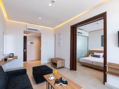 Helles Wohnzimmer mit schwarzem Sofa, Holztisch und angrenzendem Schlafzimmer mit braunem Bett.