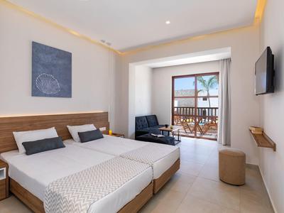 Helles Hotelzimmer mit zwei Betten, Balkon, Fernseher und moderner Einrichtung in neutralen Farben.