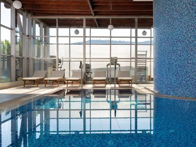 Moderner Innenpool mit blauer Mosaikwand, großen Fenstern und Holzdeck mit Liegestühlen.