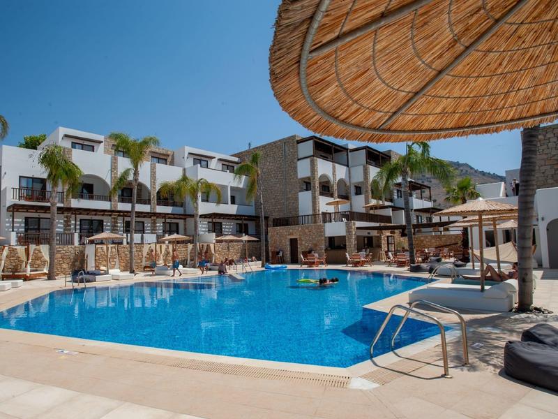 Área de piscina de hotel moderna con tumbonas, palmeras y sombrillas bajo un cielo despejado.