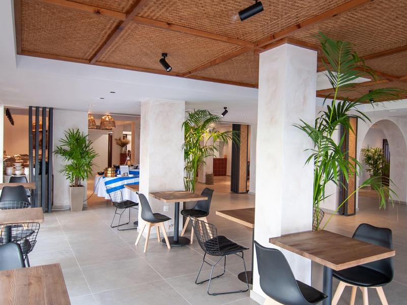 Restaurante de hotel luminoso con sillas modernas, mesas y arreglos de plantas.