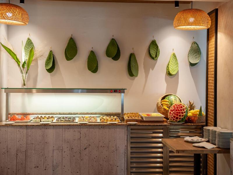 Zona de buffet con frutas, pasteles y hojas decorativas en la pared de un restaurante del hotel.
