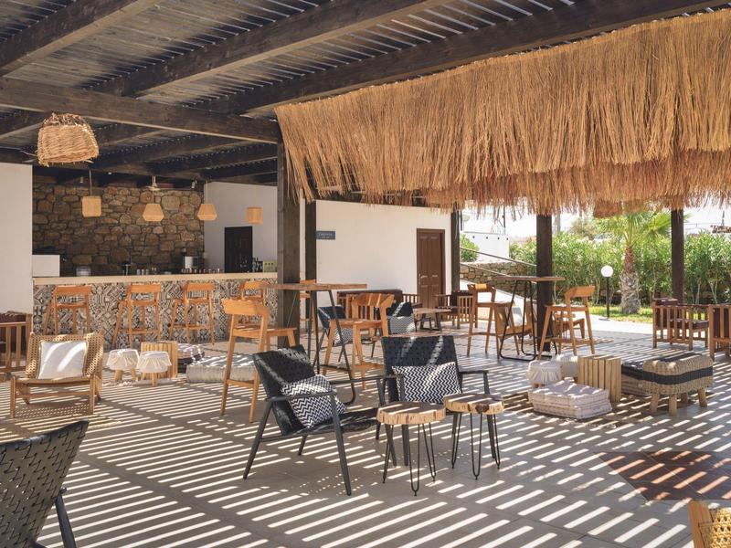 Área lounge abierta con sillas, mesas y luz natural bajo un techo de paja.