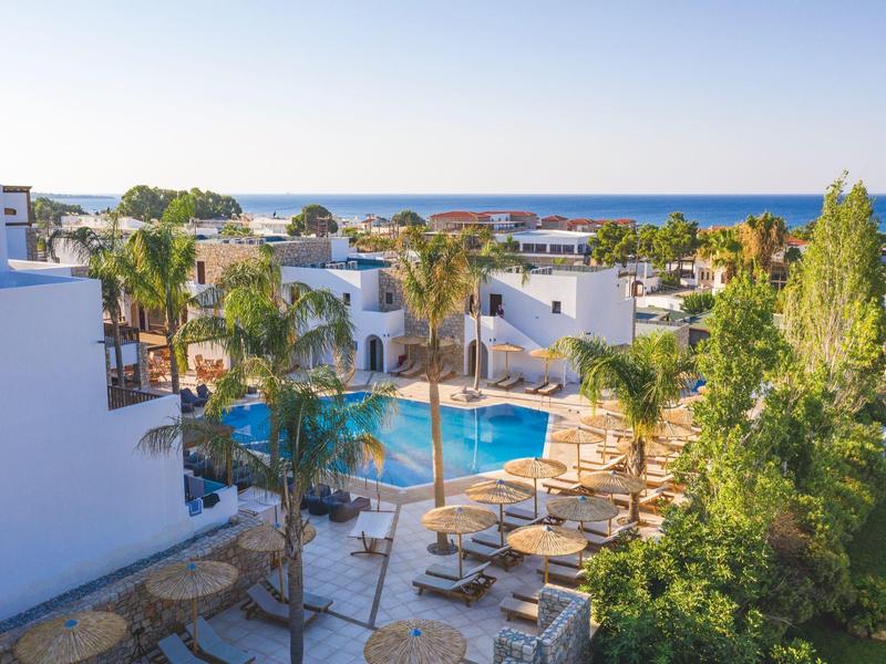 Complejo hotelero con piscina, palmeras y edificios blancos cerca del mar con cielo despejado.