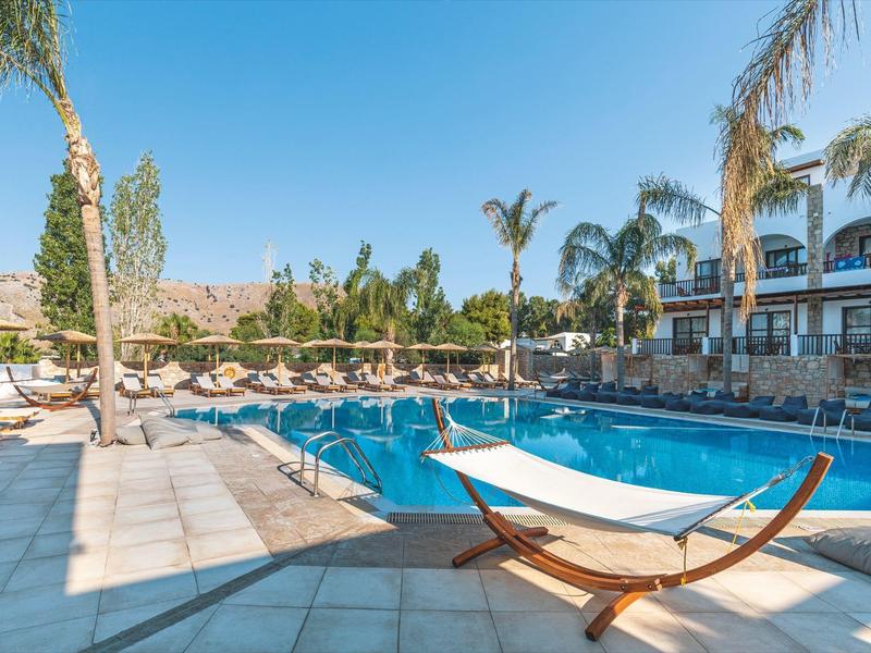 Piscina moderna de hotel con tumbonas, palmeras y cielo despejado en un día soleado.
