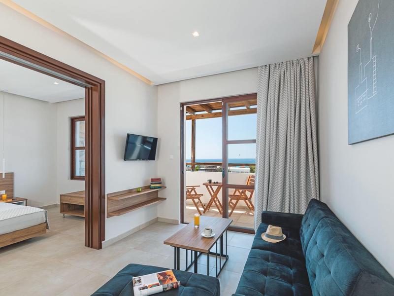 Habitación de hotel luminosa con sala integrada, balcón y vista al mar durante el día.