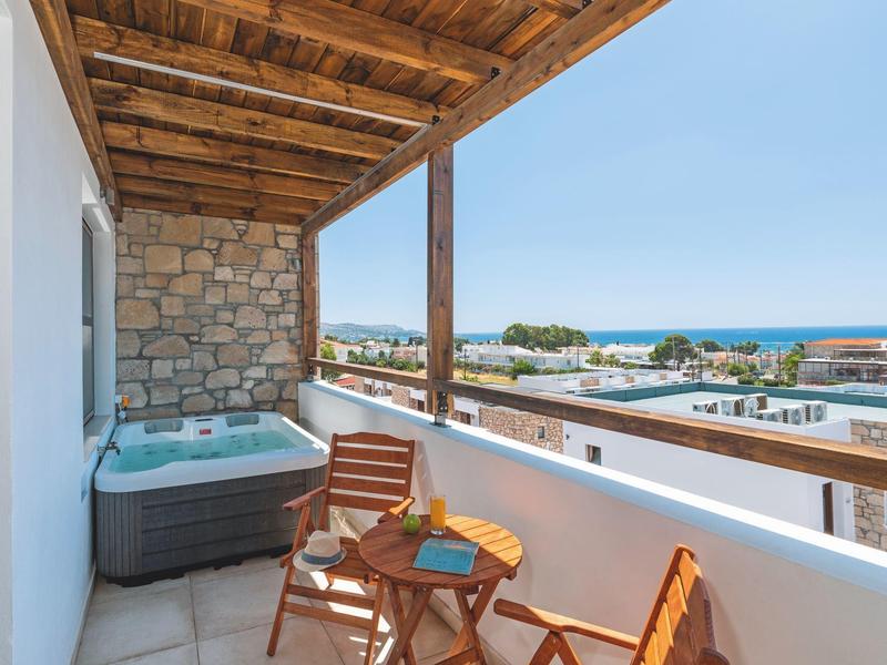 Balcón con jacuzzi, muebles de madera y vista al mar y edificios cercanos.