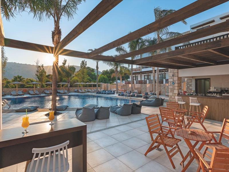 Área exterior moderna de un hotel con piscina, sombra y asientos al atardecer.