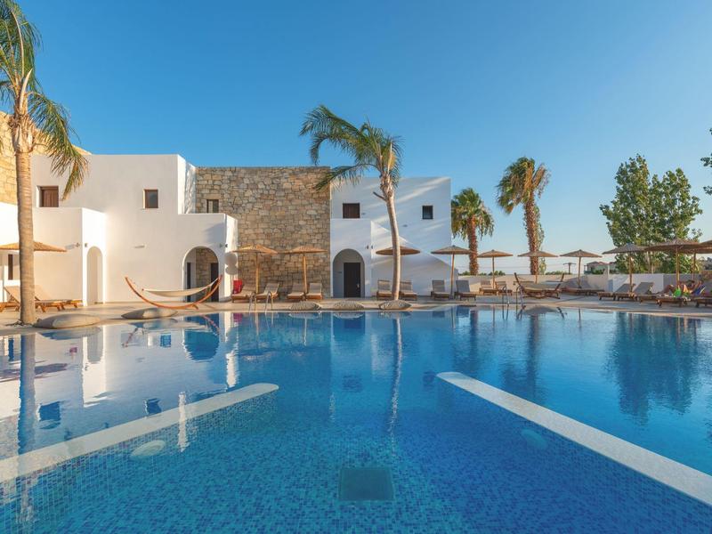 Piscina grande con agua azul frente a un hotel blanco con palmeras bajo un cielo despejado