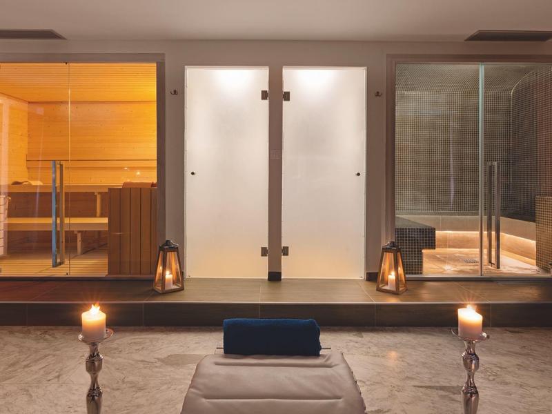 Área de bienestar moderna con sauna, baño de vapor y horno de sauna, velas y toalla al frente.