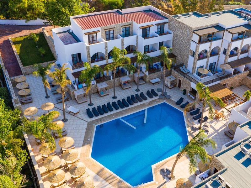 Vista aérea de un hotel con gran piscina, tumbonas y palmeras, rodeado de vegetación exuberante.