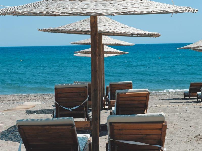 Tumbonas de madera bajo sombrillas de paja en una playa con mar azul y cielo despejado.