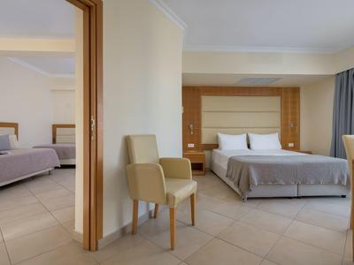 Moderne hotelkamer met een bed, stoelen, tegelvloer en een verbindingsdeur naar een andere kamer.