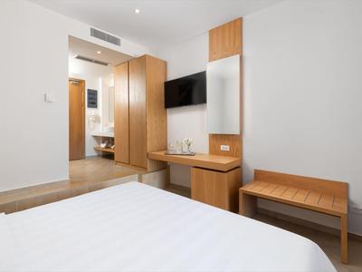 Minimalistische hotelkamer met wit beddengoed, houten meubels en een aan de muur gemonteerde tv.