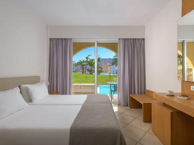 Moderne hotelkamer met twee bedden, een bureau en een raam met uitzicht op een zwembad en groen.