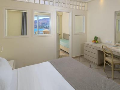 Lichte hotelkamer met wit beddengoed, bureau met stoel en raam met uitzicht op bergen.