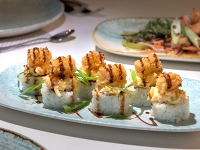 Gegrilde garnalen sushirollen geserveerd op een rechthoekig wit bord met garnering.