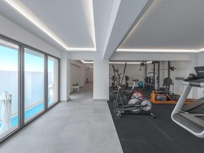 Salle de sport lumineuse avec équipements modernes et grandes fenêtres donnant sur la piscine.