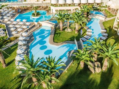 Modern hotelgebouw bij de zee met palmbomen en bergen op de achtergrond.