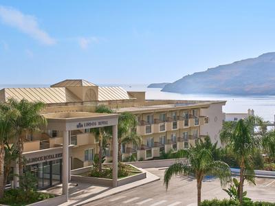 Modern hotelgebouw bij de zee met palmbomen en bergen op de achtergrond.