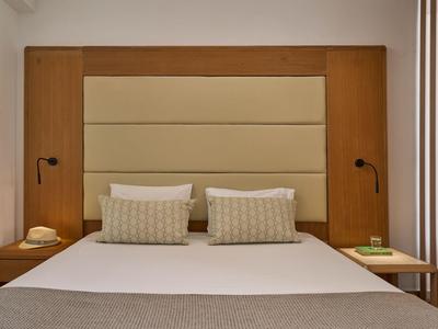 Moderne hotelkamer met een groot bed, gestoffeerd hoofdeinde, nachtlampjes en houten nachtkastjes.