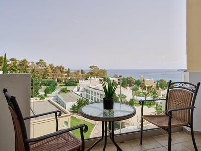 Balkon met een kleine tafel en twee stoelen met uitzicht op een hotel tuin en zeezicht.