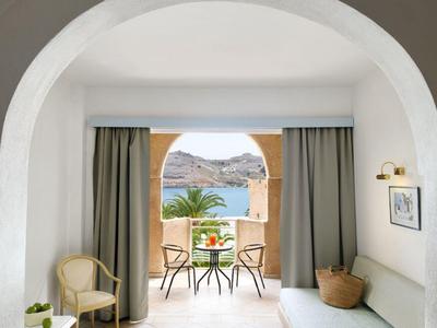 Uitzicht door een boog naar een balkon met tafel en stoelen met uitzicht op bergen en zee.