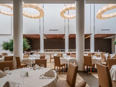 Restaurant élégant avec tables rondes, chaises confortables et grandes fenêtres dans un cadre lumineux.