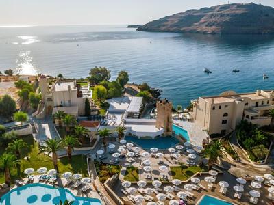 Resort met zwembaden en ligstoelen aan zee, met een rotsachtige kustlijn op de achtergrond.