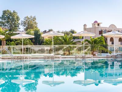 Une zone de piscine calme avec des parasols blancs devant un hôtel méditerranéen.