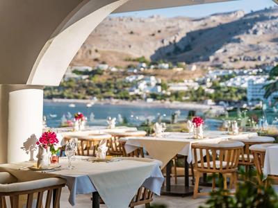 Buitenterras met gedekte tafels, uitzicht op water en heuvels bij zonnig weer.