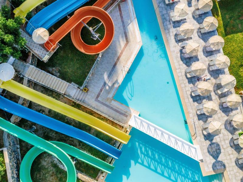 Bovenaanzicht van een kleurrijk glijbaangebied naast een zwembad met ligstoelen en parasols.