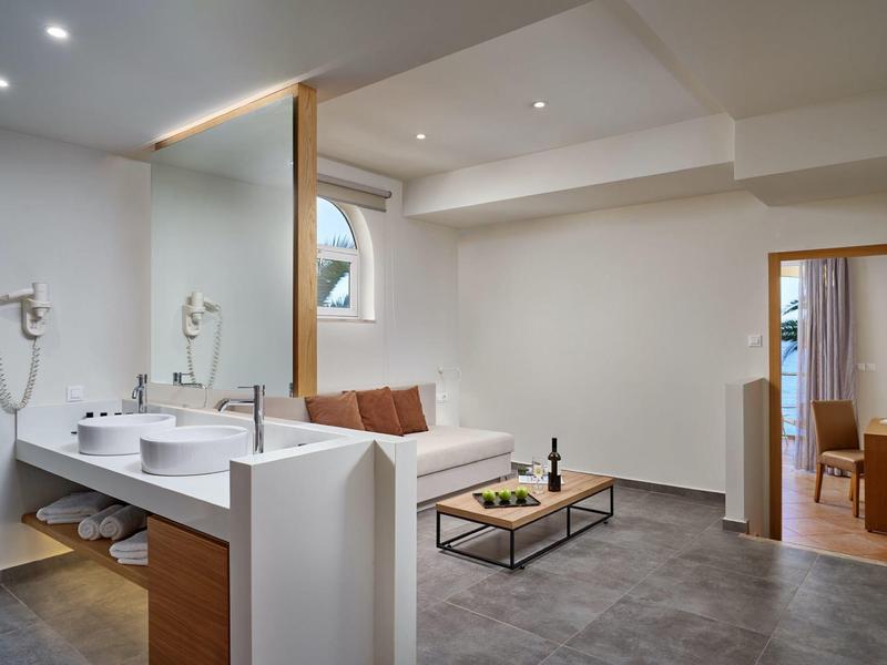 Moderne open hotelkamer met badkamer en gezellige zithoek met bank en salontafel.