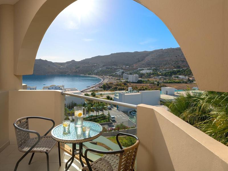 Balkon met tafel en stoelen met uitzicht op een strand en kustplaats bij een heldere hemel.